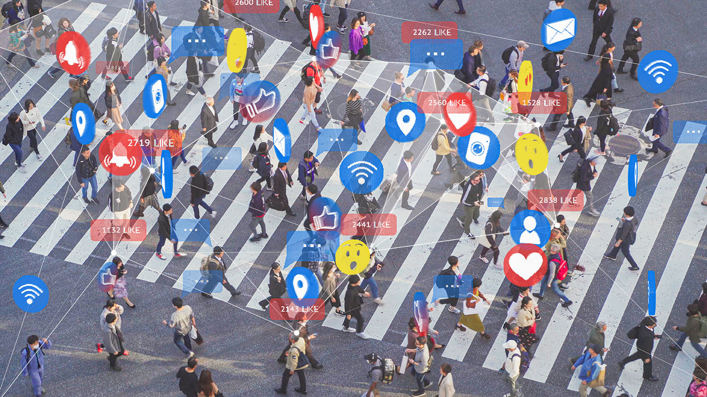 A crowd of people cross a busy city intersection with social media graphics around them to indicate busy online activity